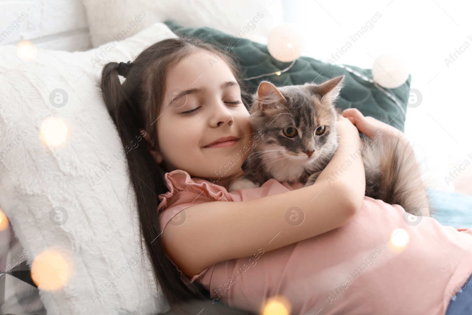 Photo of Cute little girl with cat lying on bed at home