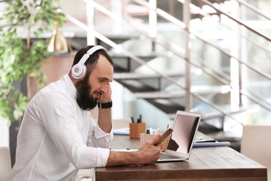 Photo of Mature man with headphones and laptop working in home office