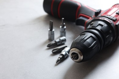 Photo of Modern electric screwdriver and bits on grey table, closeup. Space for text