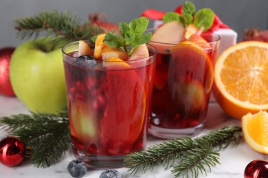 Aromatic Sangria drink in glasses, ingredients and Christmas decor on white marble table