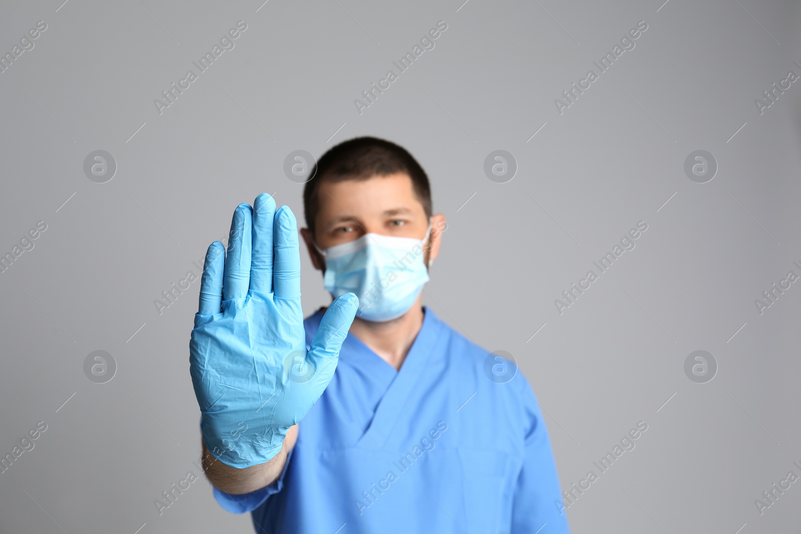 Photo of Doctor in protective mask showing stop gesture on grey background. Prevent spreading of COVID‑19
