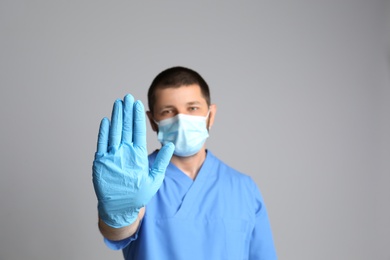 Photo of Doctor in protective mask showing stop gesture on grey background. Prevent spreading of COVID‑19