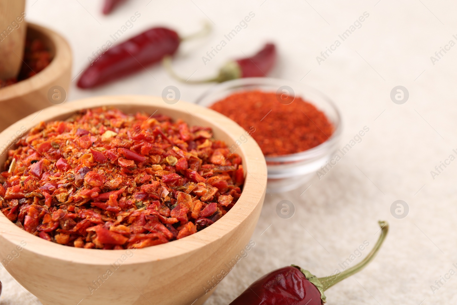 Photo of Chili pepper flakes and pods on light textured table, closeup. Space for text