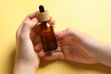 Woman holding bottle with serum on yellow background, closeup