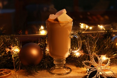 Photo of Glass of delicious hot cocoa with marshmallows and Christmas decoration on windowsill