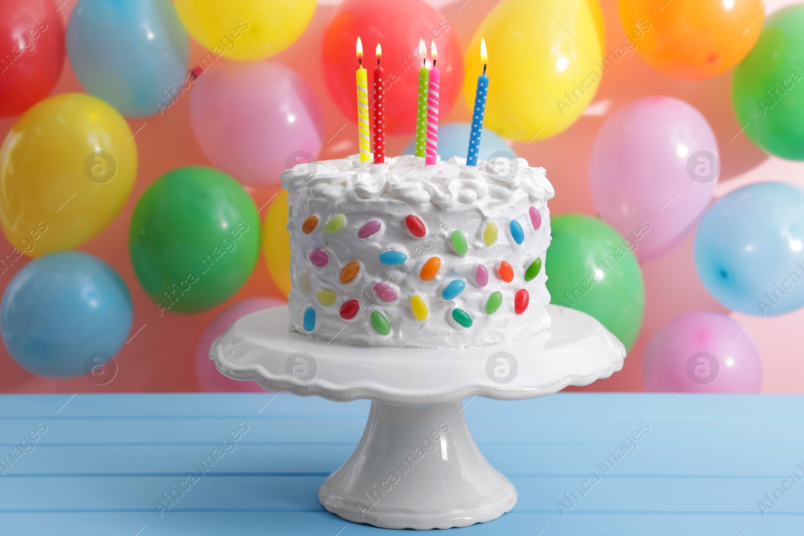 Photo of Delicious cake with cream and burning candles on light blue table