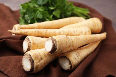 Photo of Whole raw parsley roots and fresh herb on brown fabric, closeup