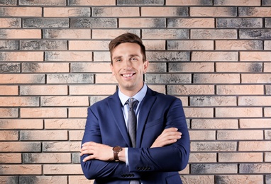 Photo of Handsome young man in suit near brick wall background