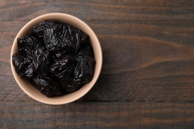 Photo of Sweet dried prunes in bowl on wooden table, top view. Space for text