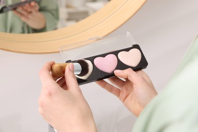 Photo of Woman with blusher and brush near mirror indoors, closeup