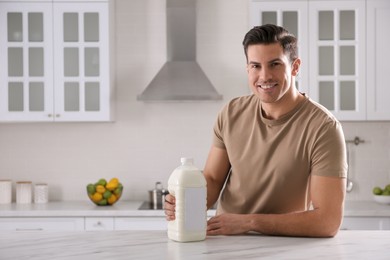 Photo of Man with gallon bottle of milk at white marble table in kitchen. Space for text