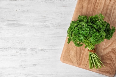 Photo of Board with fresh green parsley and space for text on wooden background, top view