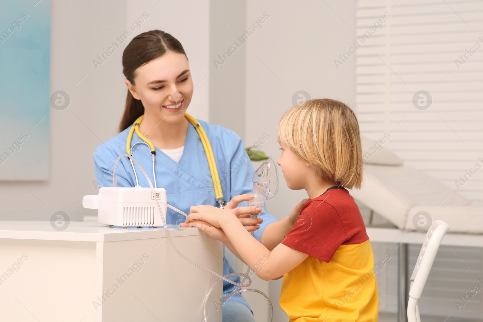 Photo of Medical assistant helping sick little boy with nebulizer inhalation at hospital