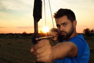 Man with bow and arrow practicing archery in field at sunset