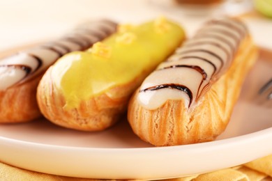 Plate with different tasty glazed eclairs on table, closeup