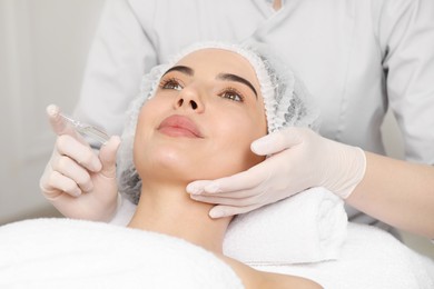 Professional cosmetologist holding skincare ampoule while working with client in clinic, closeup