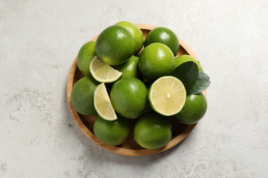 Photo of Fresh ripe limes and green leaves on light table, top view