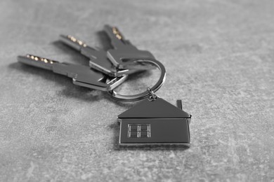 Photo of Keys with keychain in shape of house on light grey table, closeup