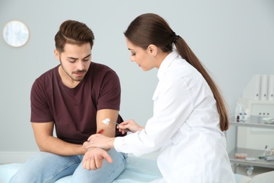 Photo of Female doctor cleaning young man's arm injury in clinic. First aid