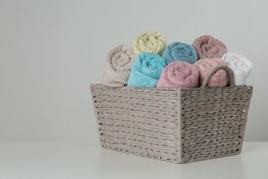 Photo of Wicker basket with clean soft towels on light background. Space for text