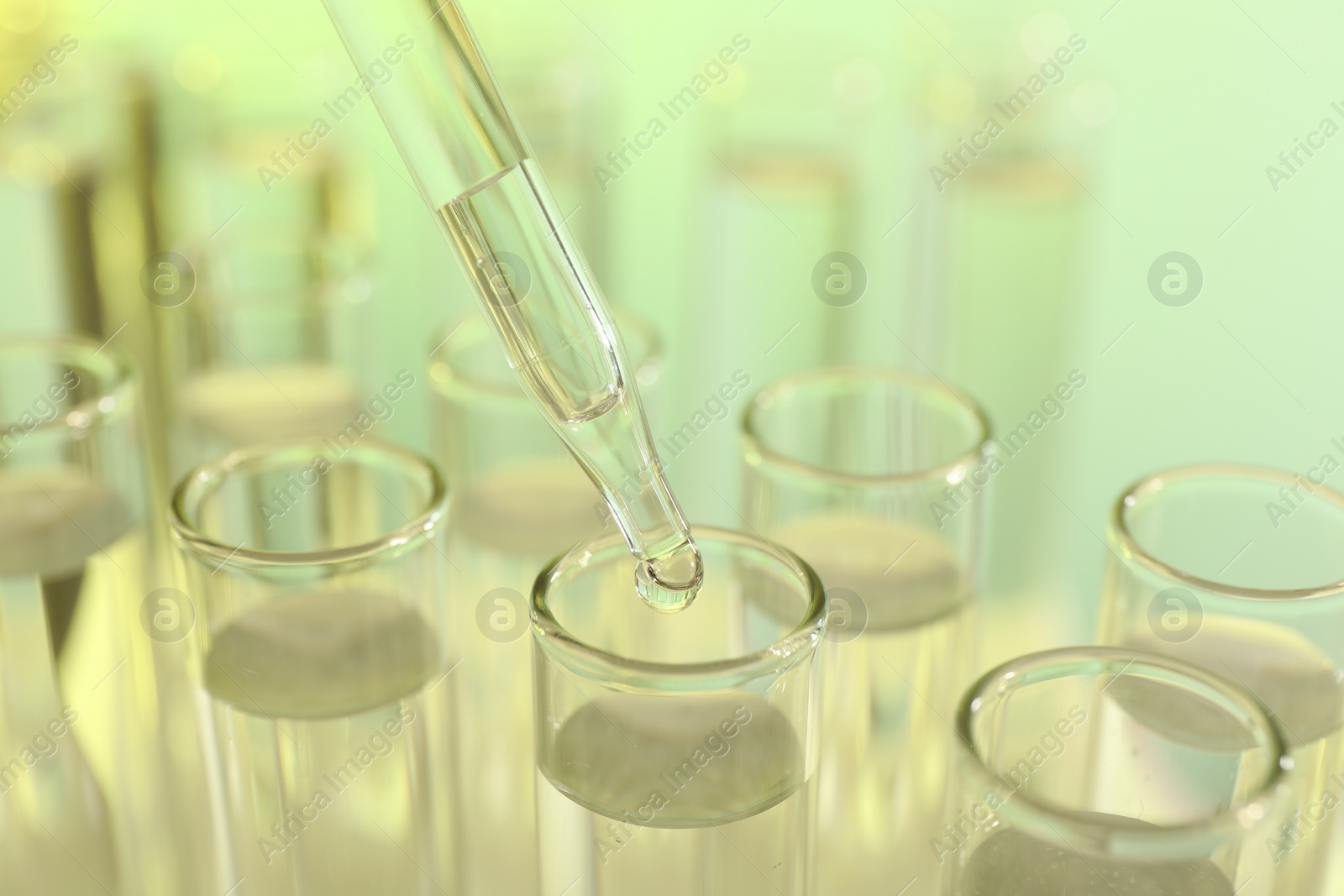 Photo of Dripping liquid from pipette into test tube on yellow background, closeup