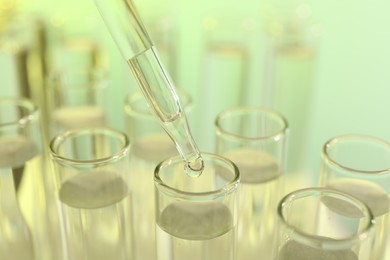 Photo of Dripping liquid from pipette into test tube on yellow background, closeup