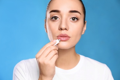 Woman with herpes applying cream on lips against light blue background