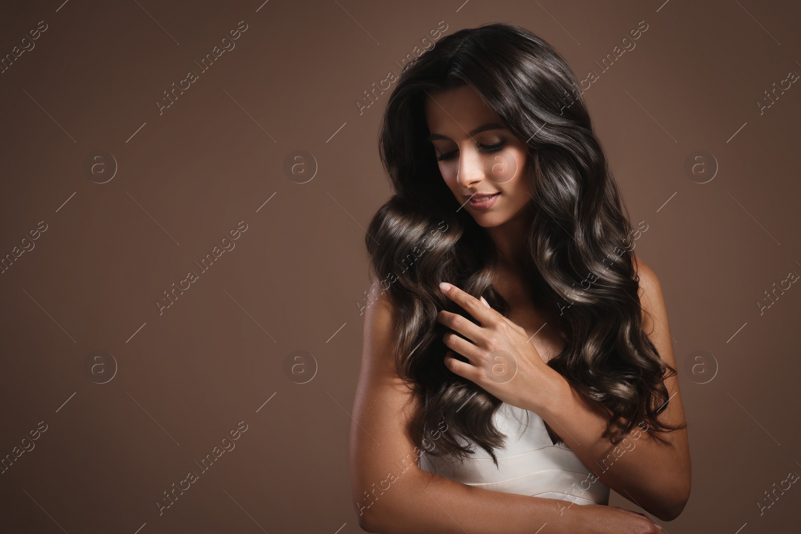 Image of Gorgeous woman with shiny wavy hair on brown background, space for text. Professional hairstyling