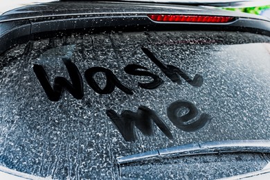 Phrase Wash Me written on dirty car window, closeup