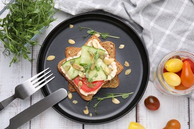 Tasty vegan sandwich with cucumber, tomato, pumpkin seeds served on white wooden table, flat lay