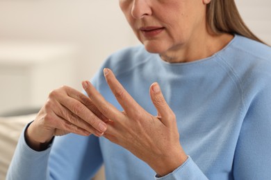 Mature woman suffering from pain in hand indoors, closeup. Rheumatism symptom