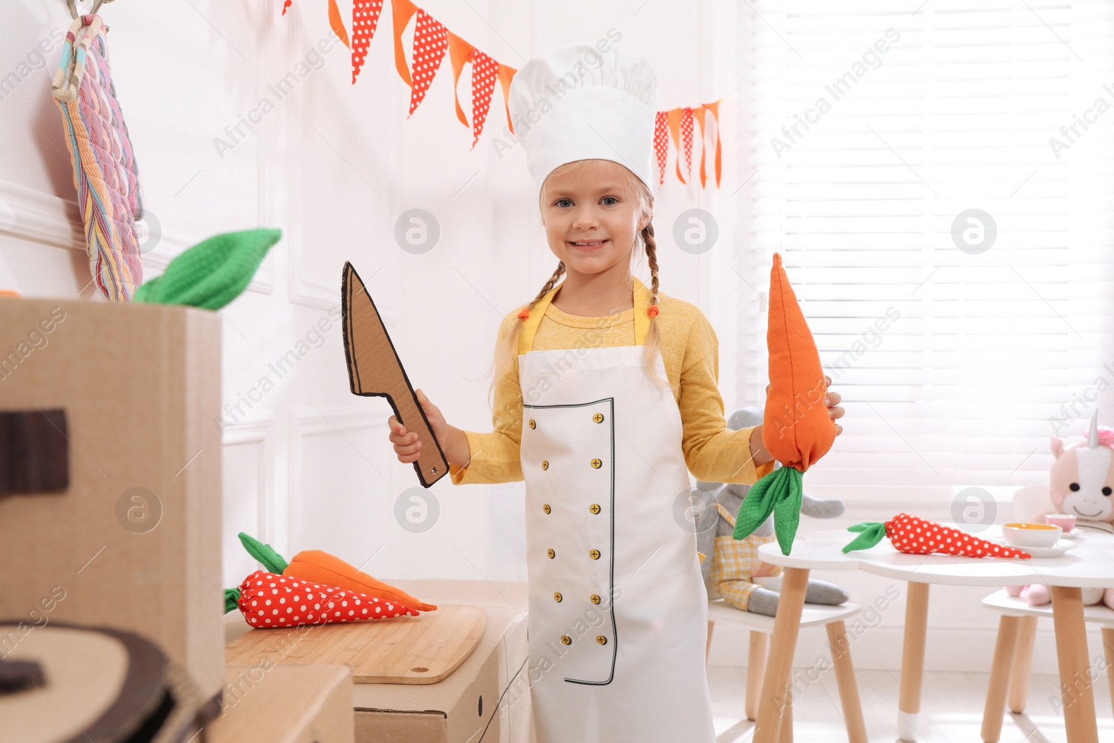 Photo of Little girl playing with toy cardboard kitchen at home