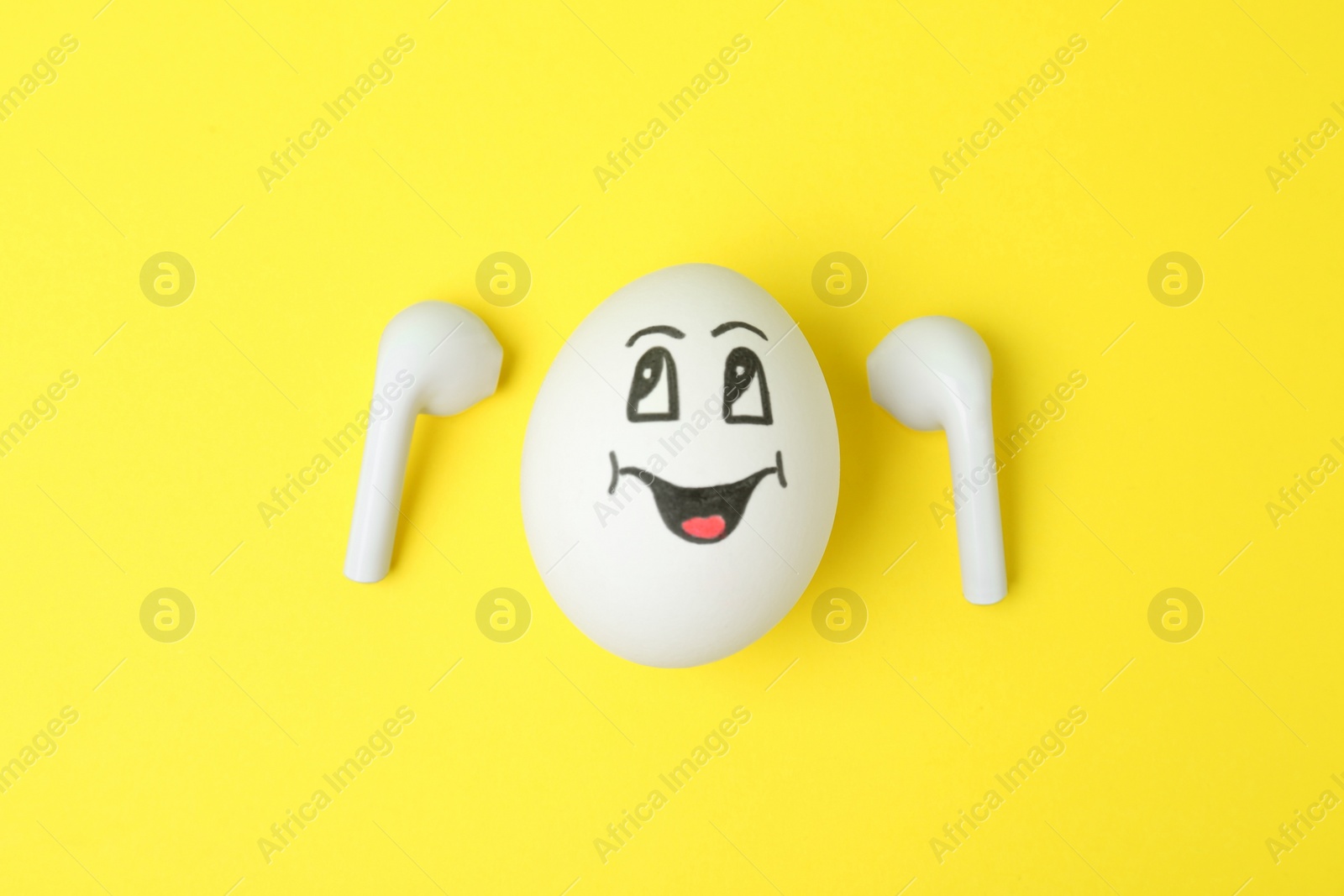 Photo of Egg with drawn happy face and earbuds on yellow background, flat lay
