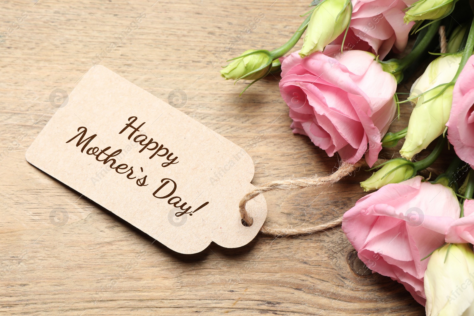 Image of Happy Mother's Day greeting label and beautiful flowers on wooden table