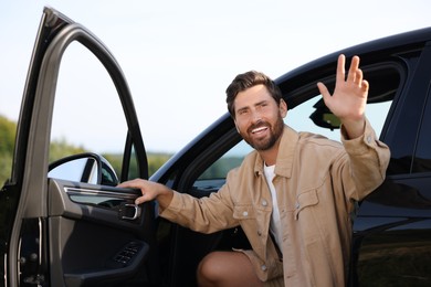 Photo of Enjoying trip. Happy bearded man waving in car