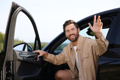 Enjoying trip. Happy bearded man waving in car