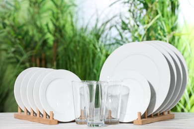 Set of clean plates and glasses on white table against blurred background