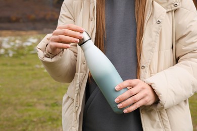 Photo of Woman holding thermo bottle in mountains, closeup
