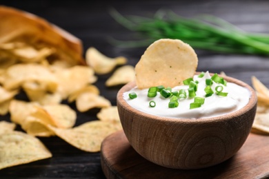 Photo of Sour cream and chips on black wooden table, closeup