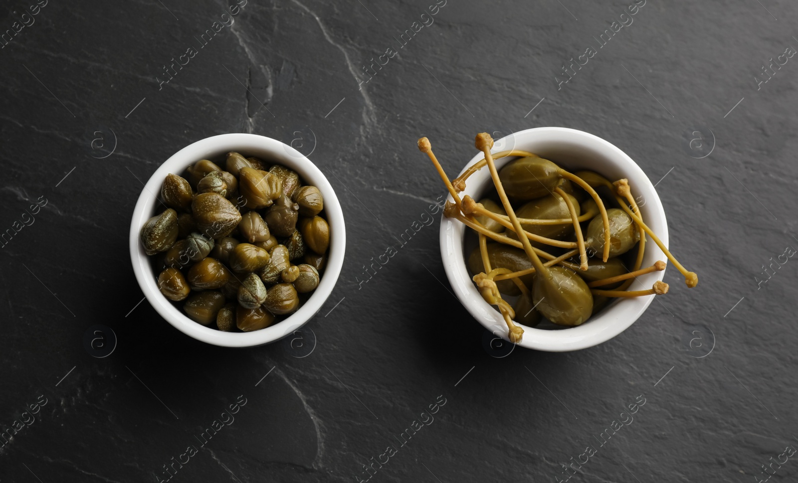 Photo of Tasty capers in bowls on black table, flat lay