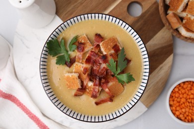 Photo of Delicious lentil soup with bacon and parsley in bowl on white table, flat lay