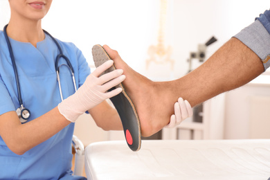 Female orthopedist fitting insole on patient's foot in clinic, closeup