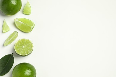 Photo of Whole and cut fresh ripe limes with green leaf on white background, flat lay