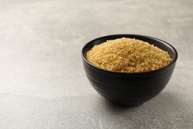 Photo of Bowl with raw bulgur on gray table, space for text