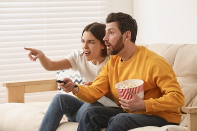 Emotional couple watching TV with popcorn on sofa