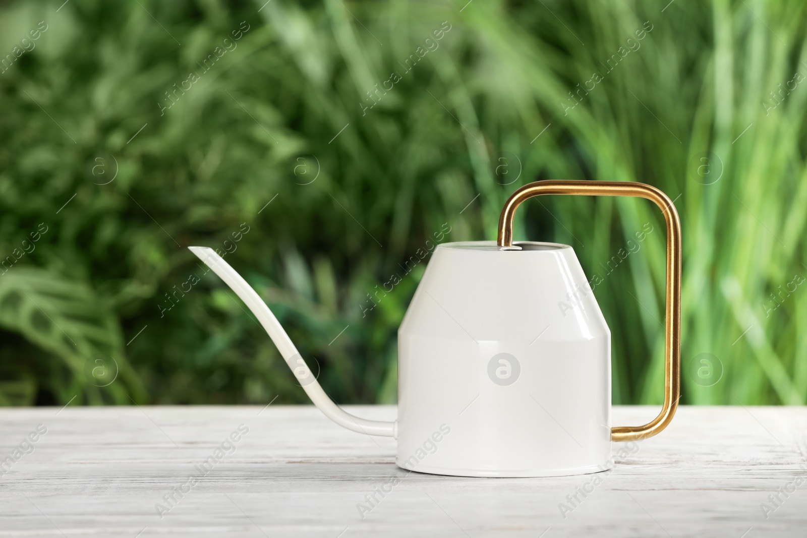 Photo of Stylish watering can on white wooden table against blurred background