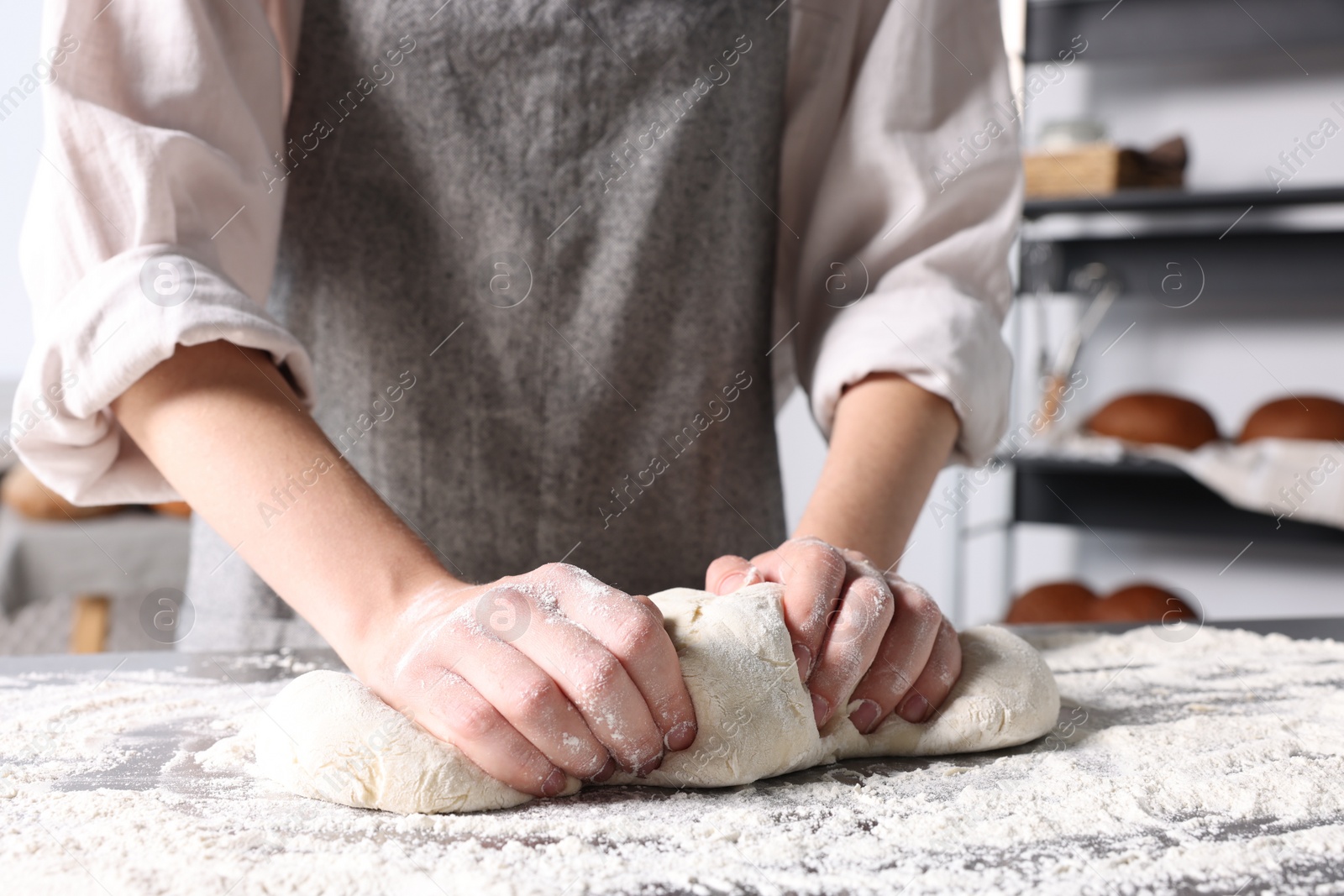 Photo of Woman kneading dough at table in kitchen, closeup