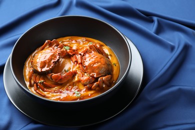 Delicious boiled crabs with sauce in bowl on blue tablecloth. Space for text