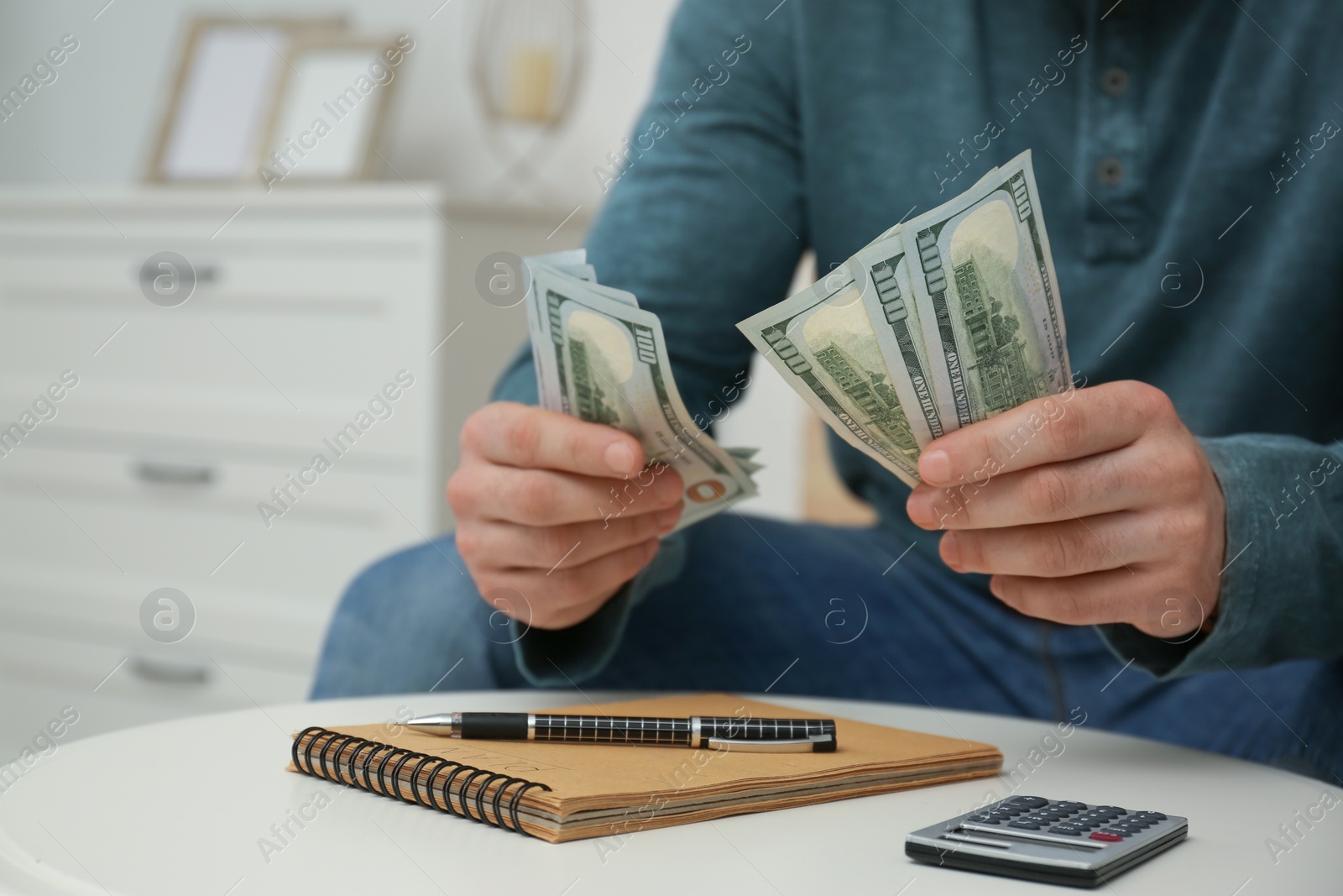 Photo of Man with money, notebook and calculator at table indoors, closeup