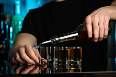 Bartender pouring alcohol drink into shot glass at mirror counter in bar, closeup